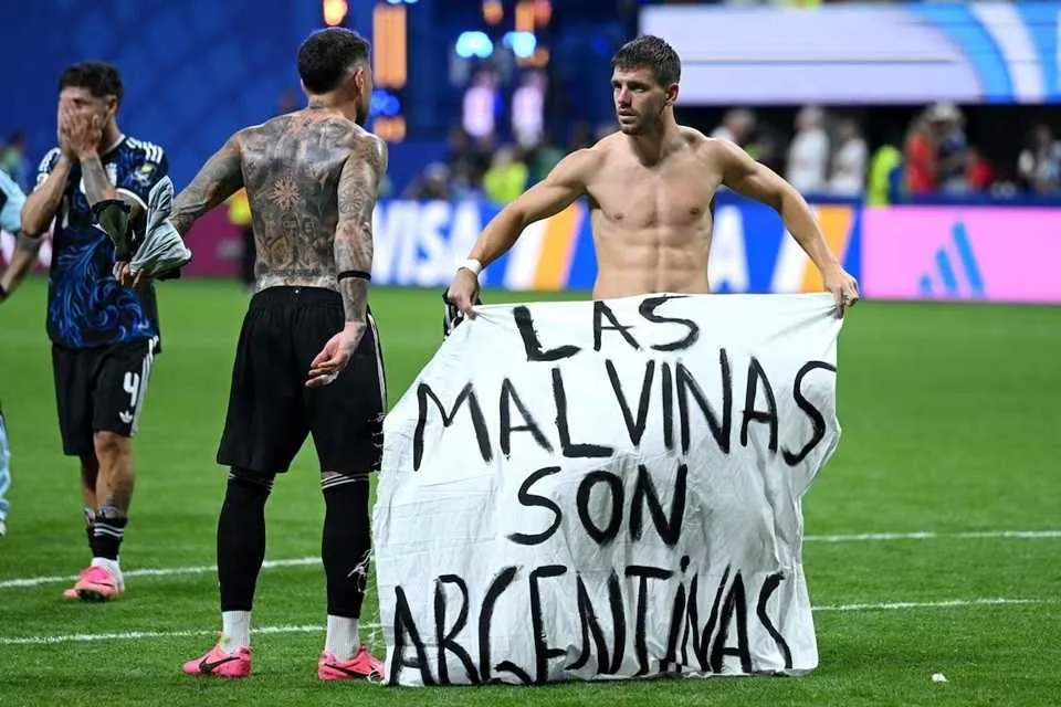 Cartel escrito a mano: Las Malvinas son argentinas, sobre el césped de un estadio